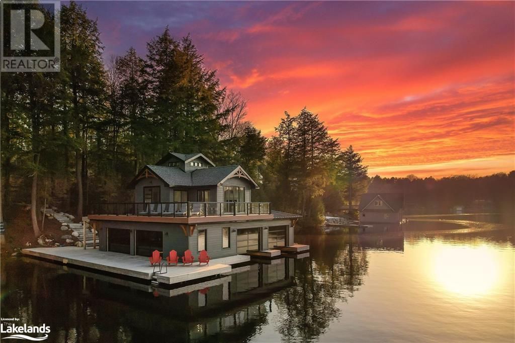 Lakeside cabin at sunset with dock and red chairs, reflecting in the water.