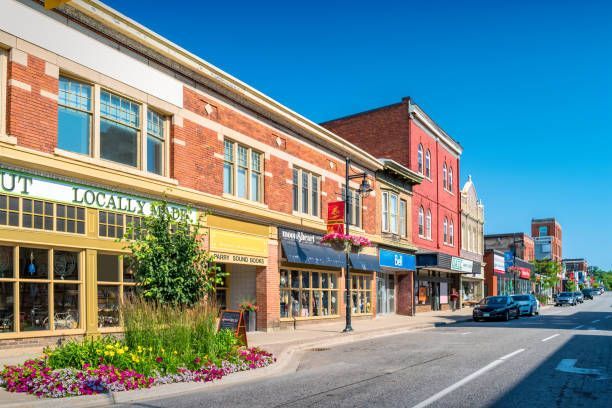 Street of shops with brick buildings, colorful awnings, and parked cars on a sunny day.