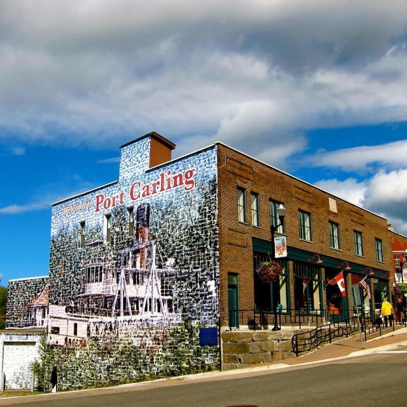 Building with mural, “Port Carling” text, blue sky, and a street.