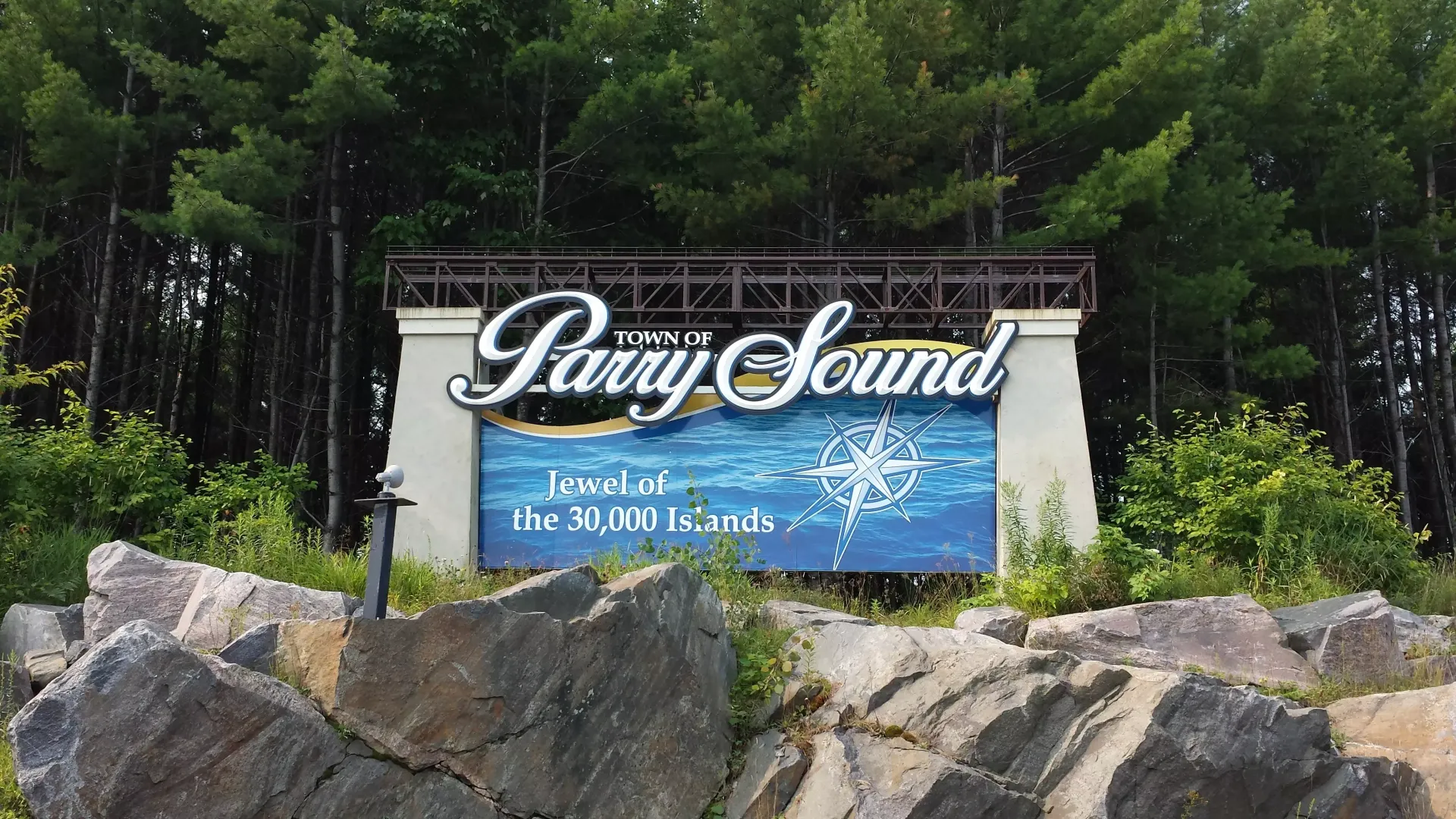 Perry Sound sign against a backdrop of trees, rocks in foreground.