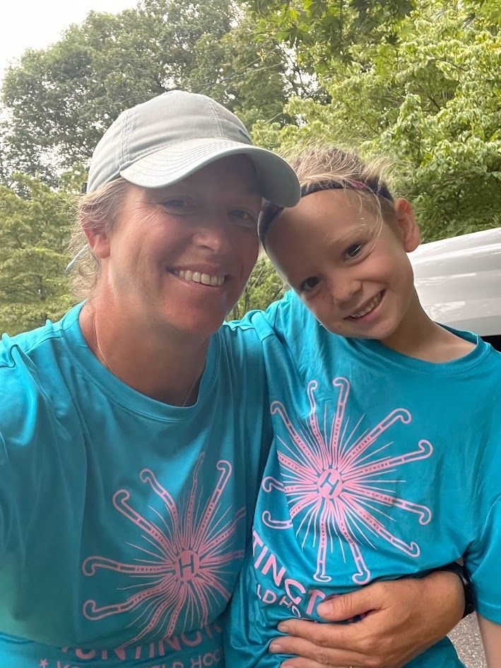 Two people in blue shirts smile outdoors in a park, with trees in the background.
