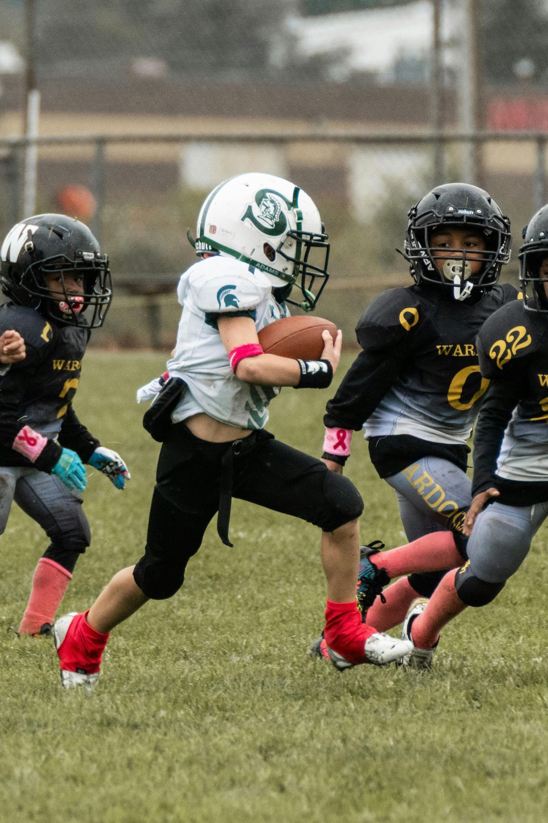 Youth football player in white sprints with the ball while defenders in black chase on a grassy field.