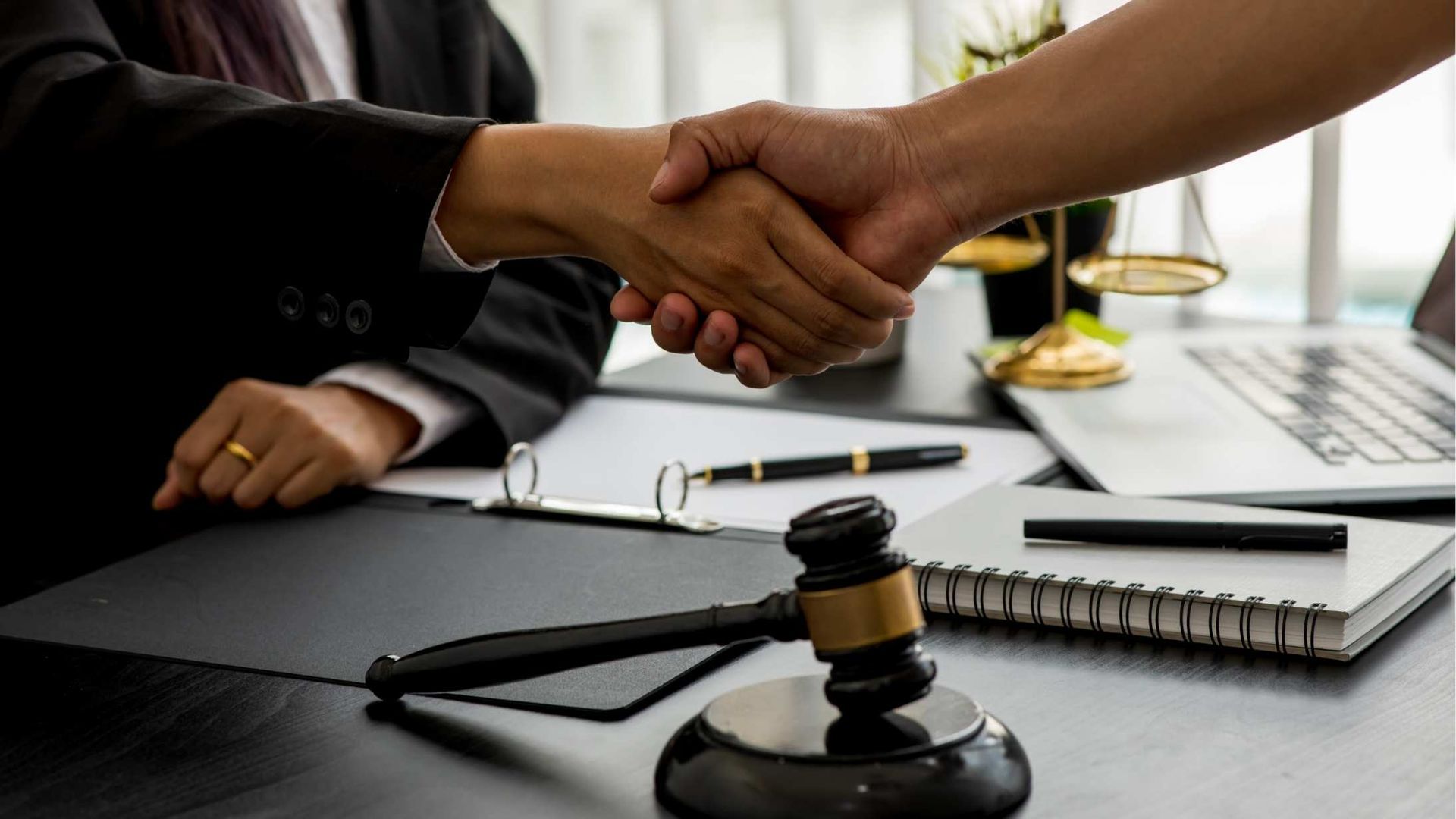 Lawyer and client shaking hands over a desk with a gavel and legal documents.