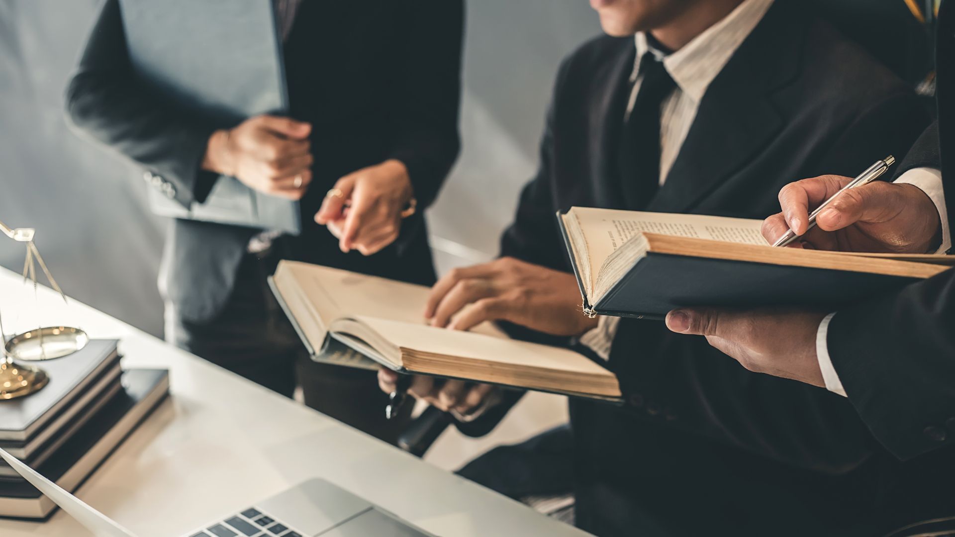 Lawyers in suits reviewing documents and discussing a case at a desk.