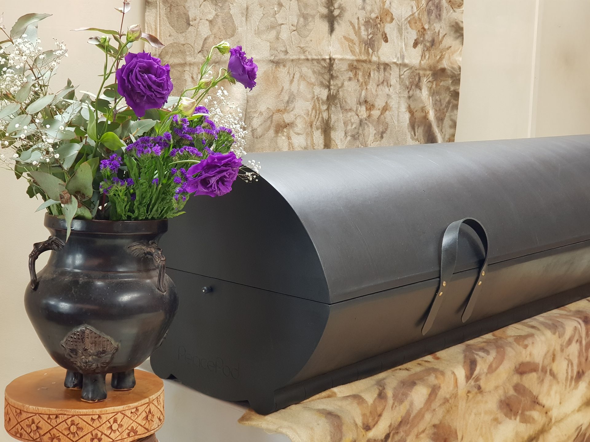 A vase of purple flowers sits next to a black coffin.