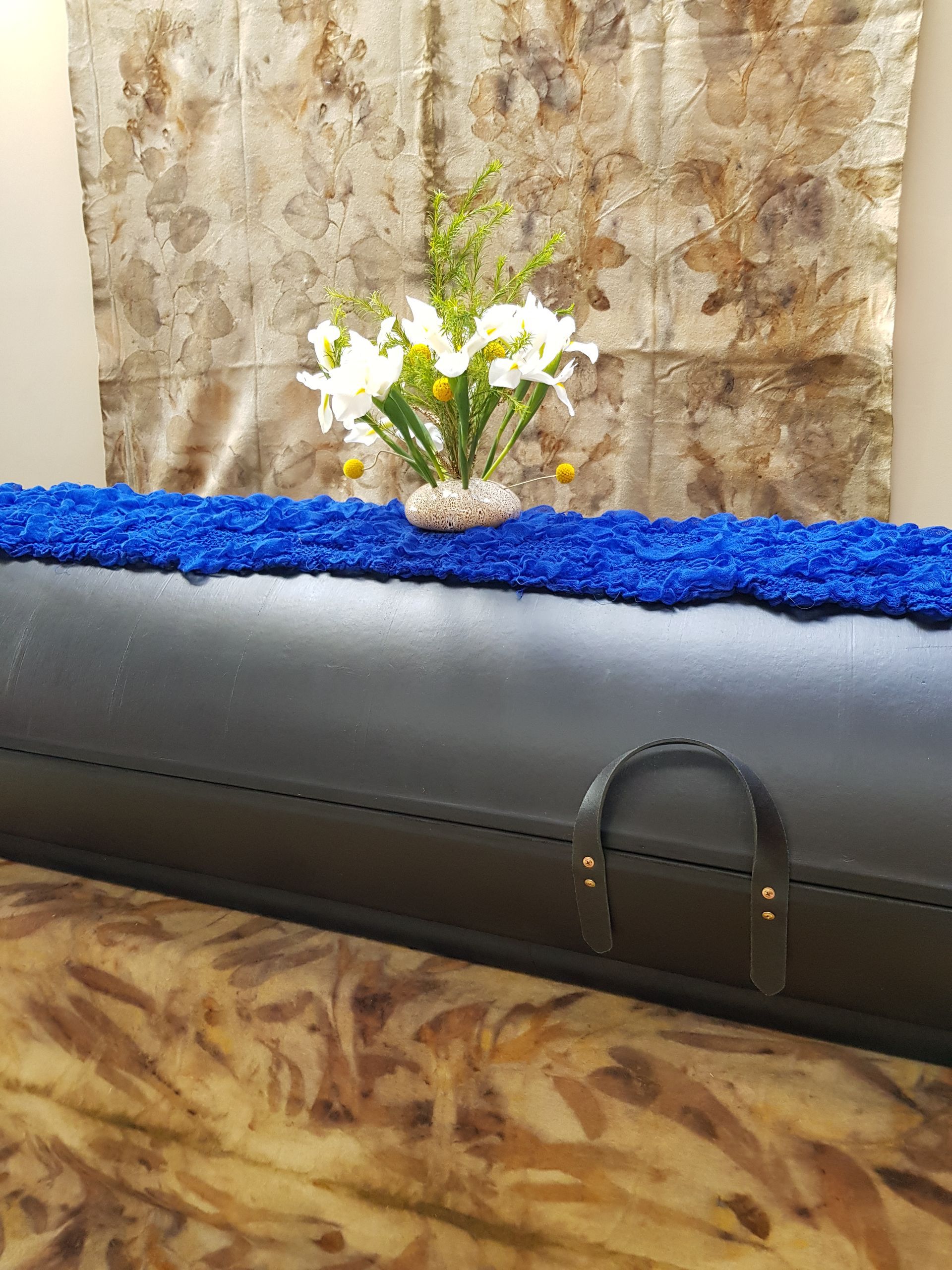 A black coffin with a vase of flowers on top of it.