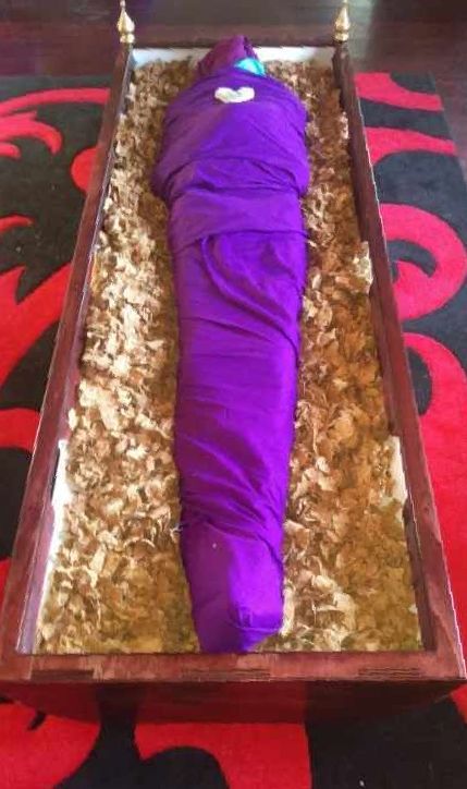 A mummy wrapped in purple cloth is laying in a PeacePod shroud bearer.