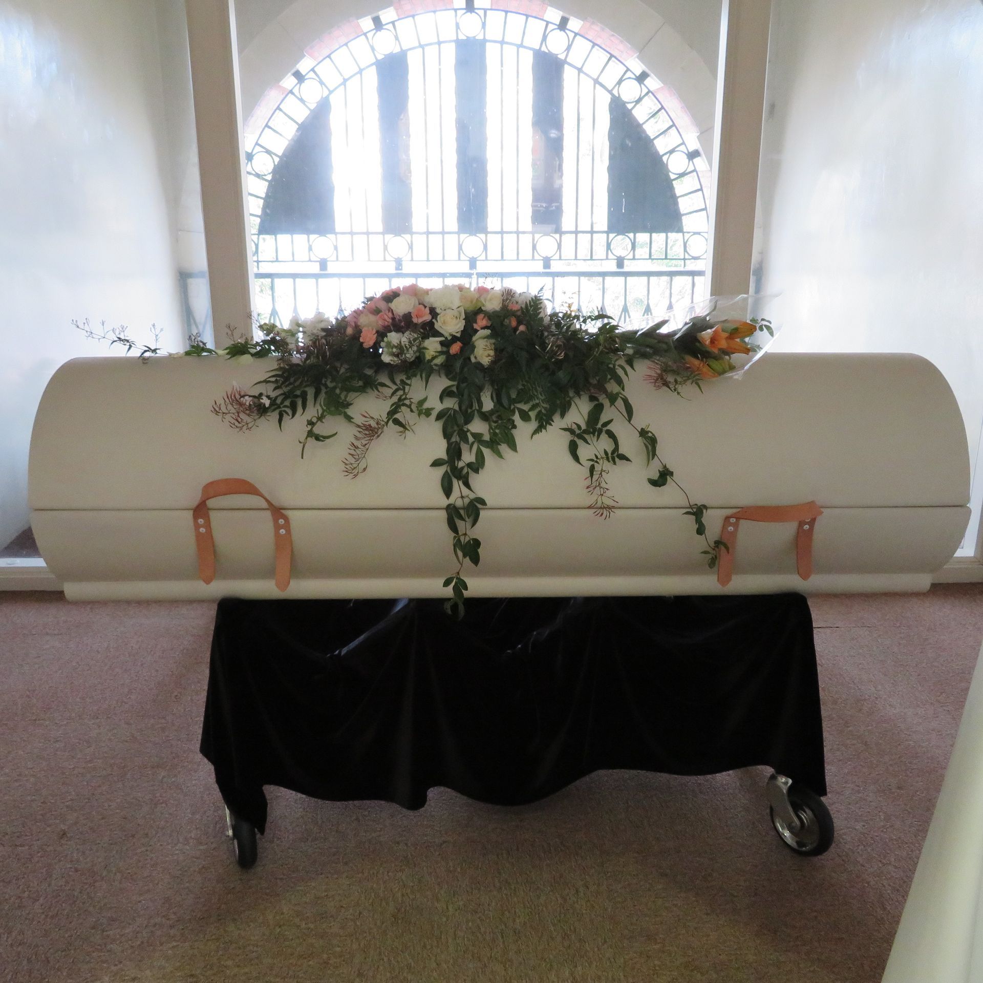 A white coffin with flowers in front of a window