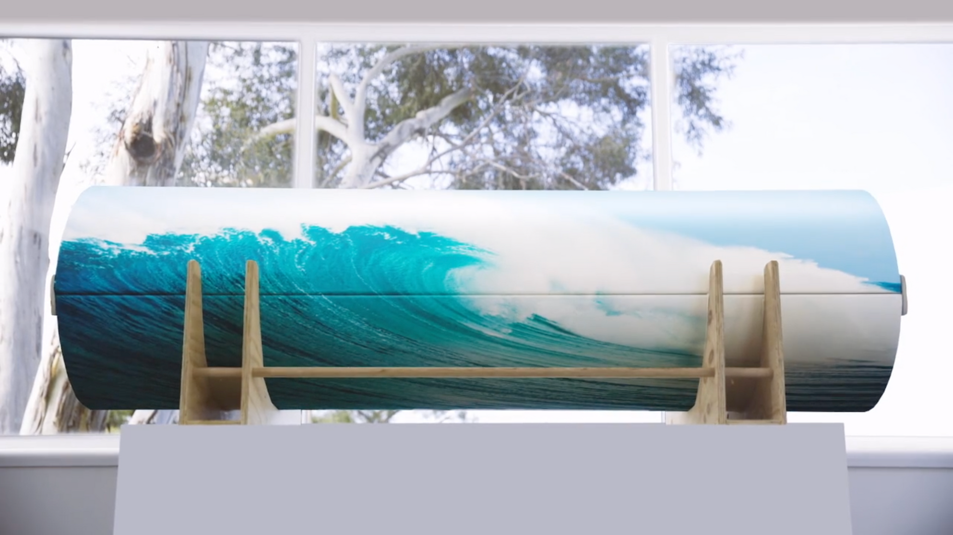 A PeacePod casket coffin with a picture of a wave on it sitting in front of a window.