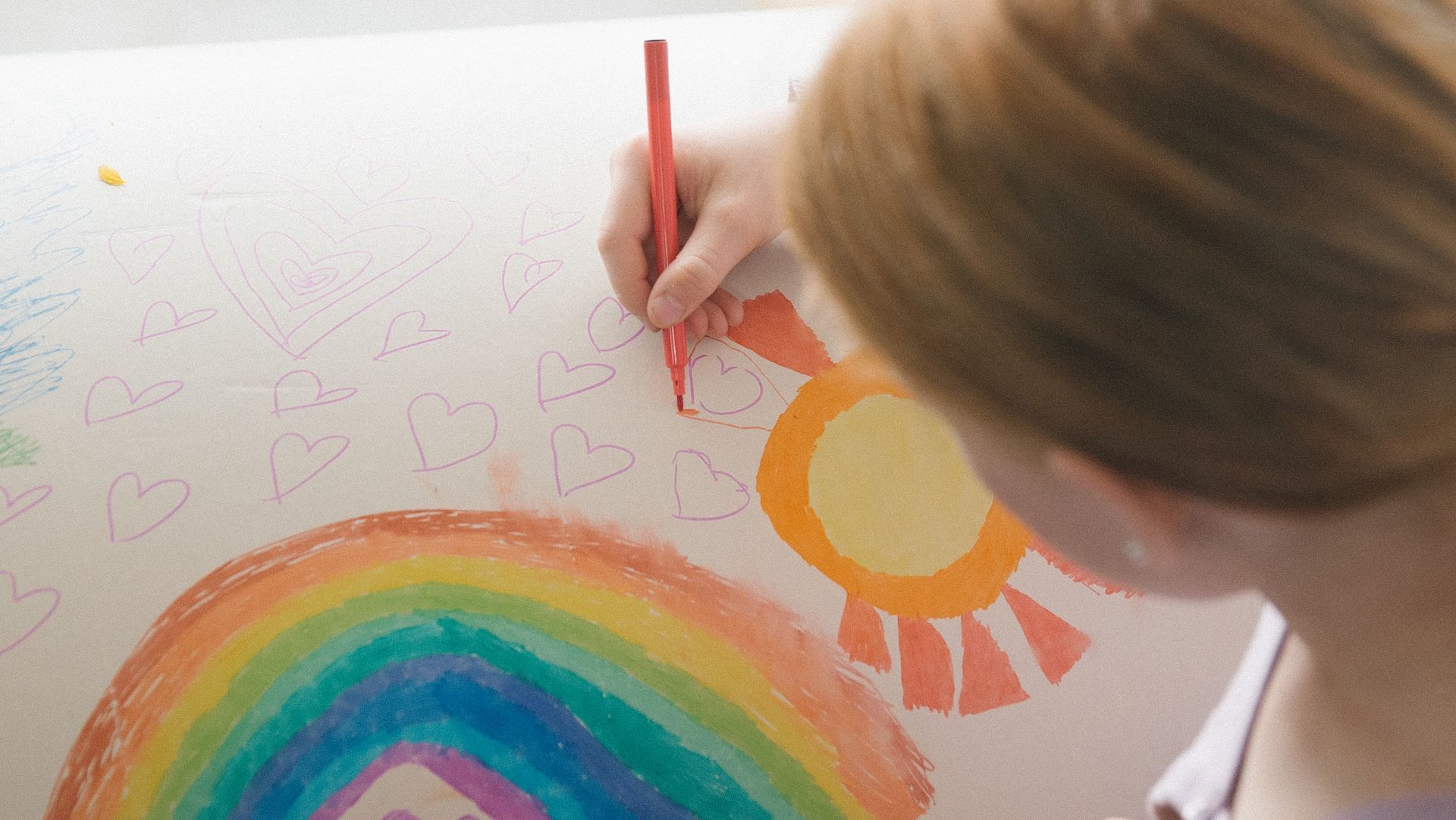 A young girl is drawing a rainbow and sun on a PeacePod cardboard casket.
