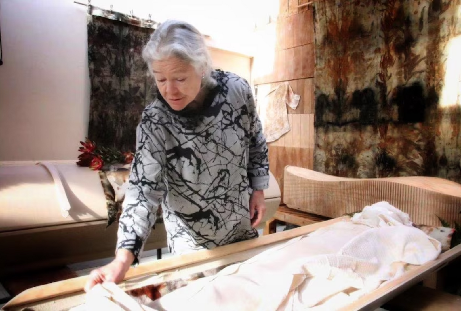 A woman is standing next to a coffin shroud carriage in a room.