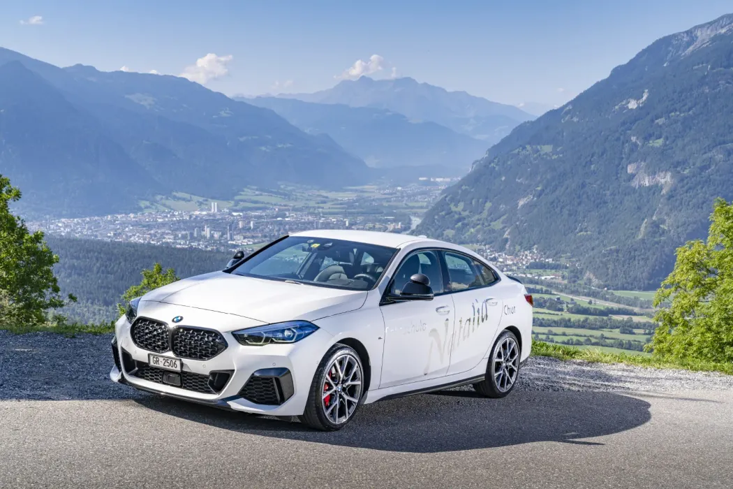 ein weißer bmw steht auf einer bergstraße im Hintergrund die Stadt Chur
