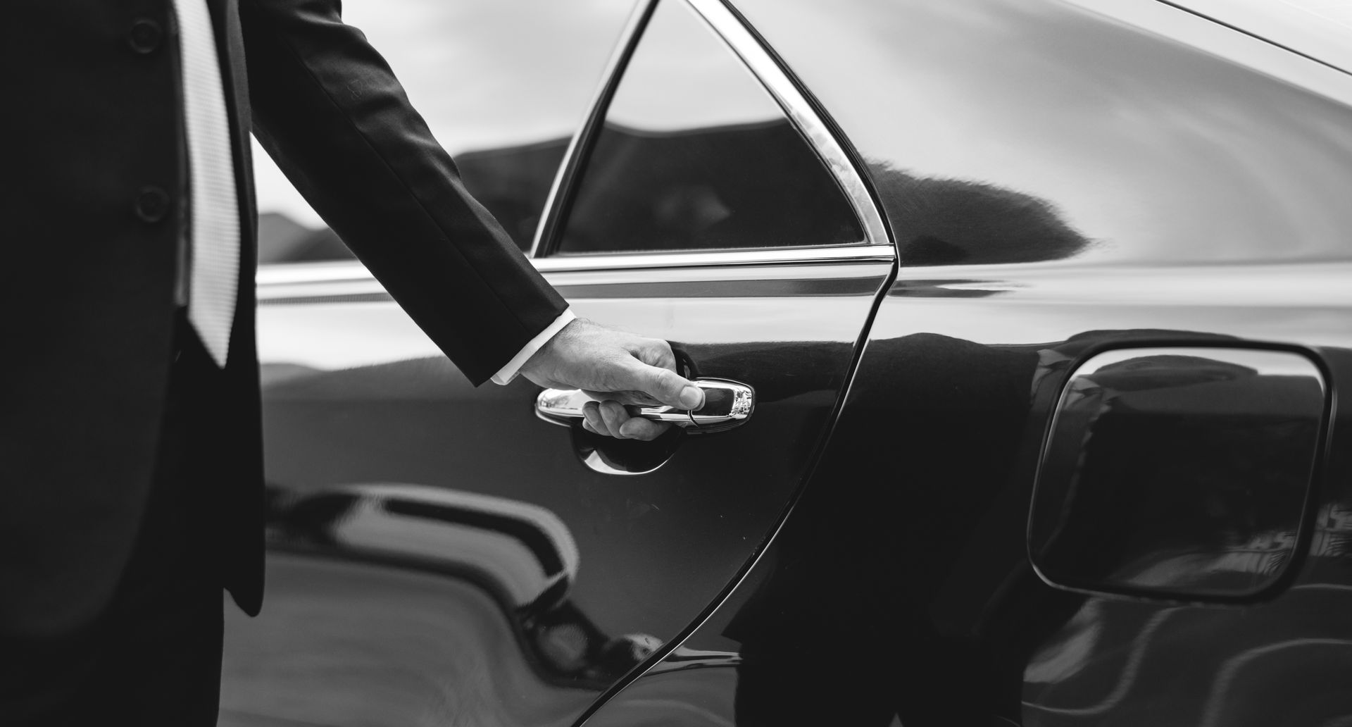 Person opening a black car door, holding the handle in a black-and-white scene