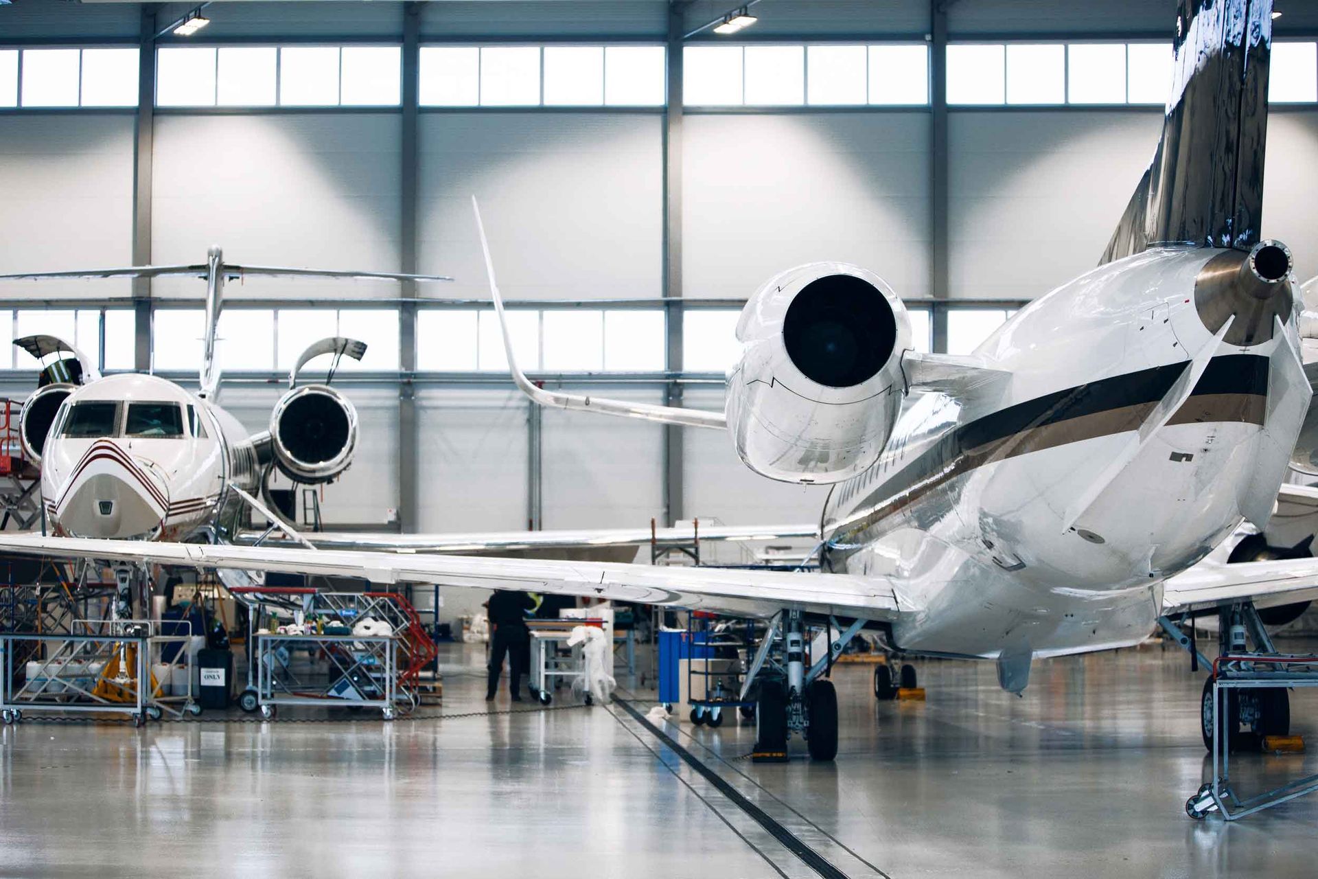 Two white private jets parked inside a hangar during maintenance