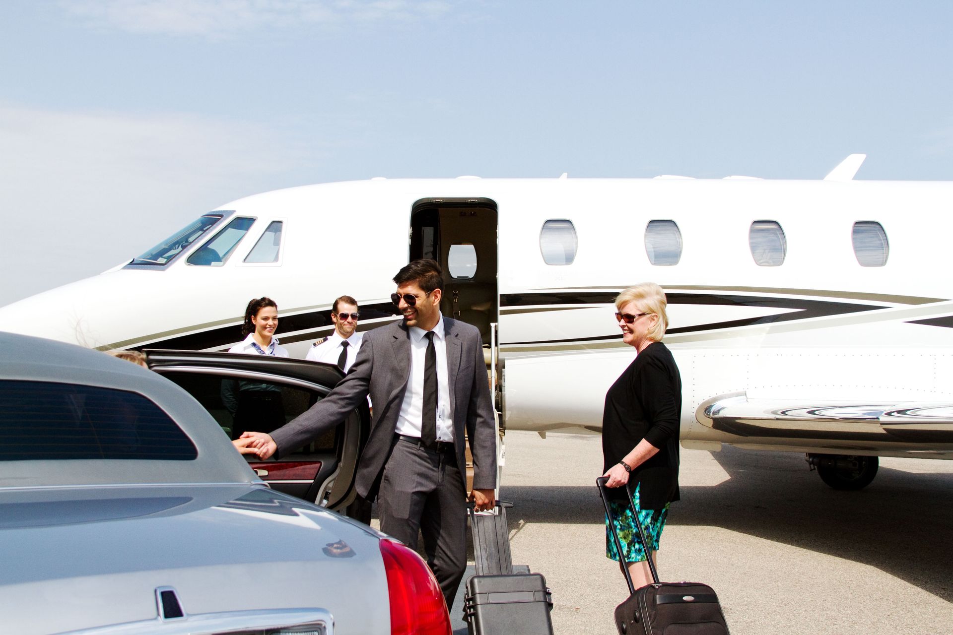 Chauffeur assisting a woman as she enters a luxury car