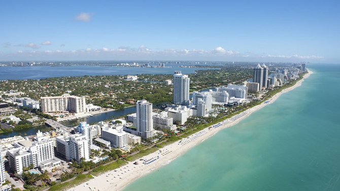 An aerial view of a city with a beach in the foreground and a body of water in the background.