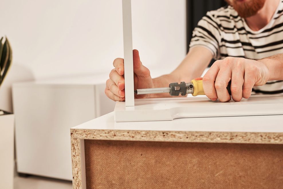 Person using a power drill to assemble a white furniture piece on a cork base