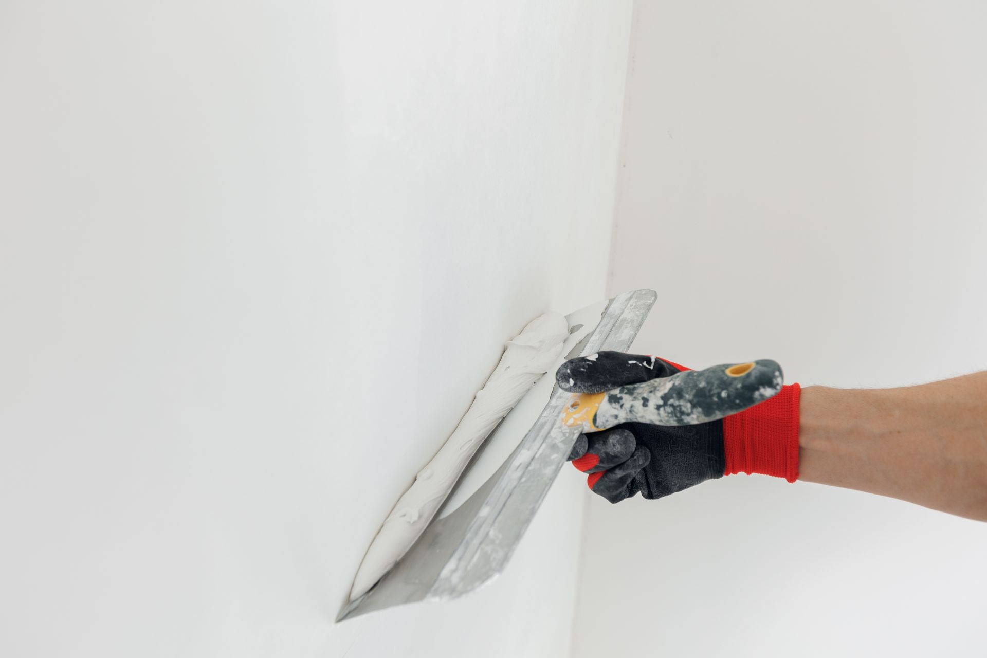Gloved hand applying gray filler or sealant to a crack in a white wall