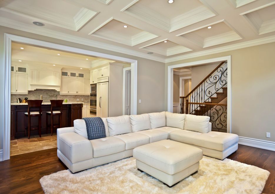 Bright open living room with white sectional, tray ceiling, and view into kitchen and staircase