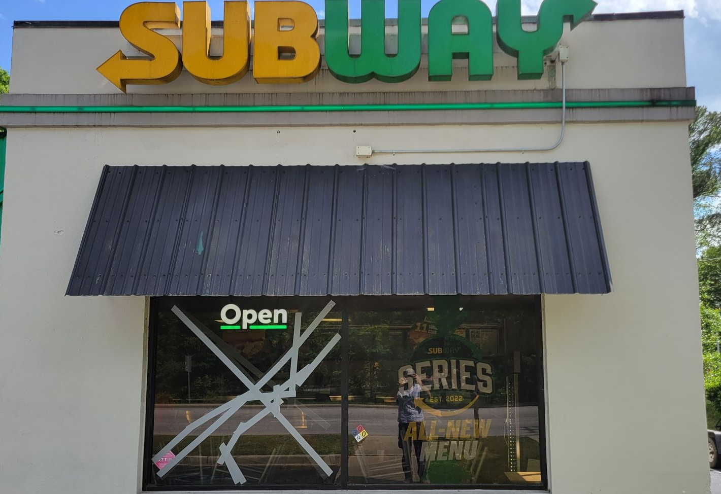 Subway storefront with green-yellow sign, black awning, and open window signage