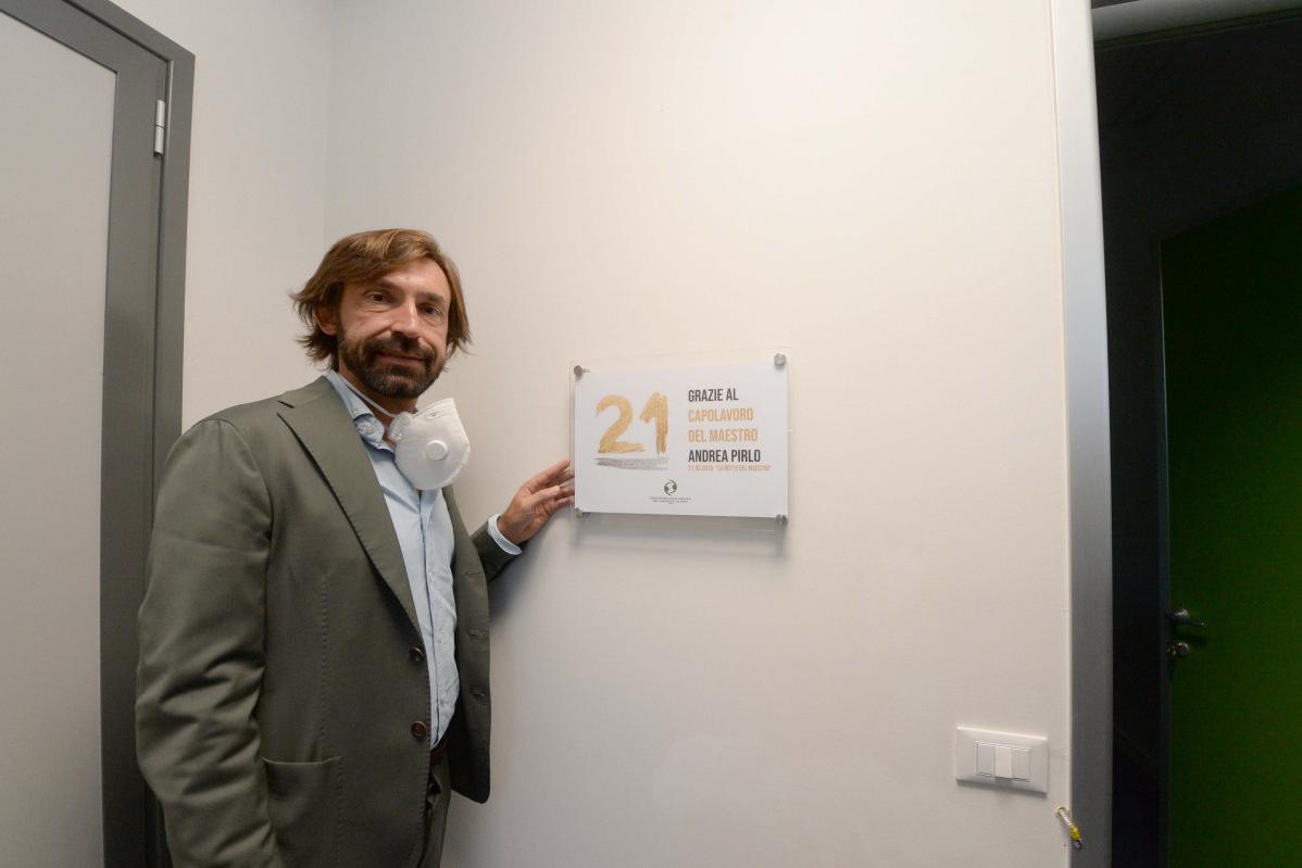 Un uomo in giacca e cravatta tiene in mano un cartello con il numero 21. È in piedi vicino a una porta.