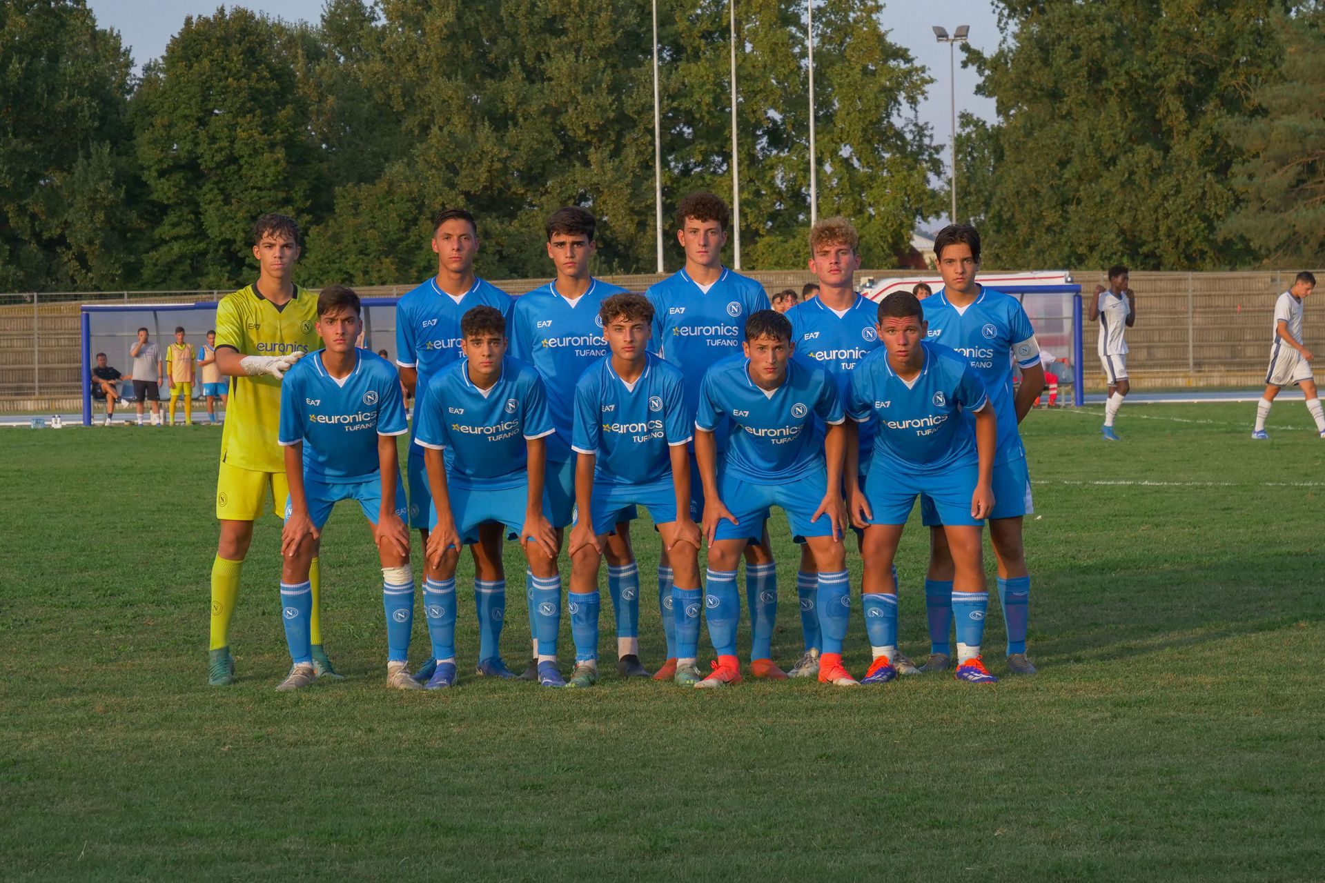 La squadra di calcio in uniforme blu posa su un campo. Un portiere indossa la divisa gialla.