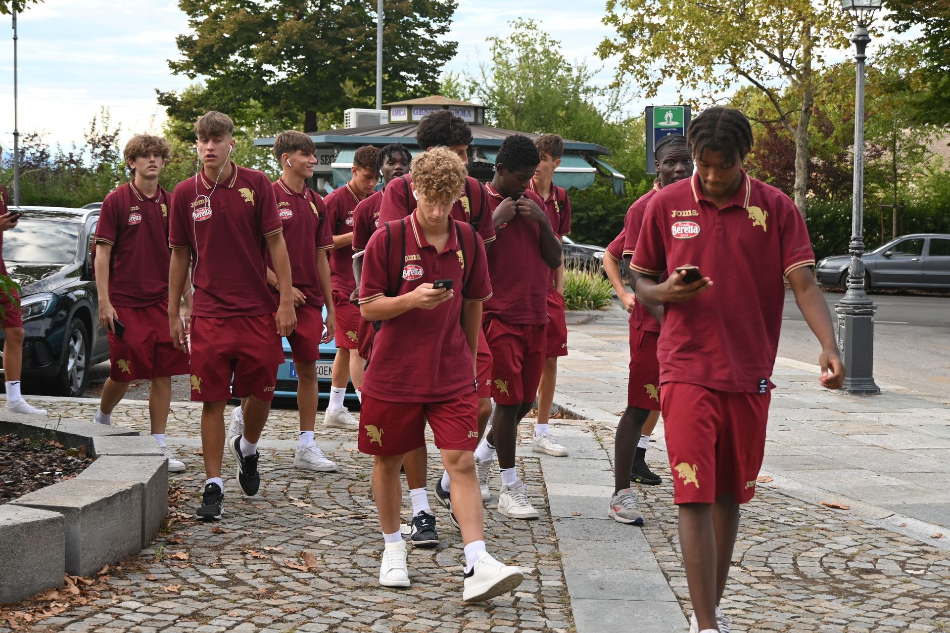 Un gruppo di giovani uomini in polo e pantaloncini color bordeaux camminano su un sentiero acciottolato.