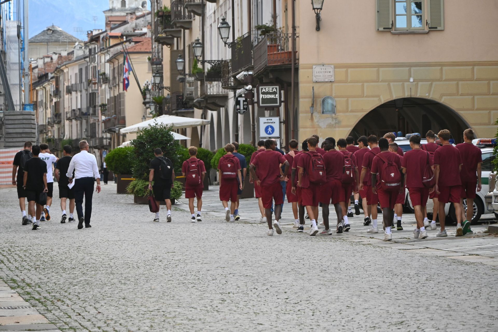 Un gruppo di persone in uniforme marrone cammina su una strada acciottolata di fronte agli edifici.