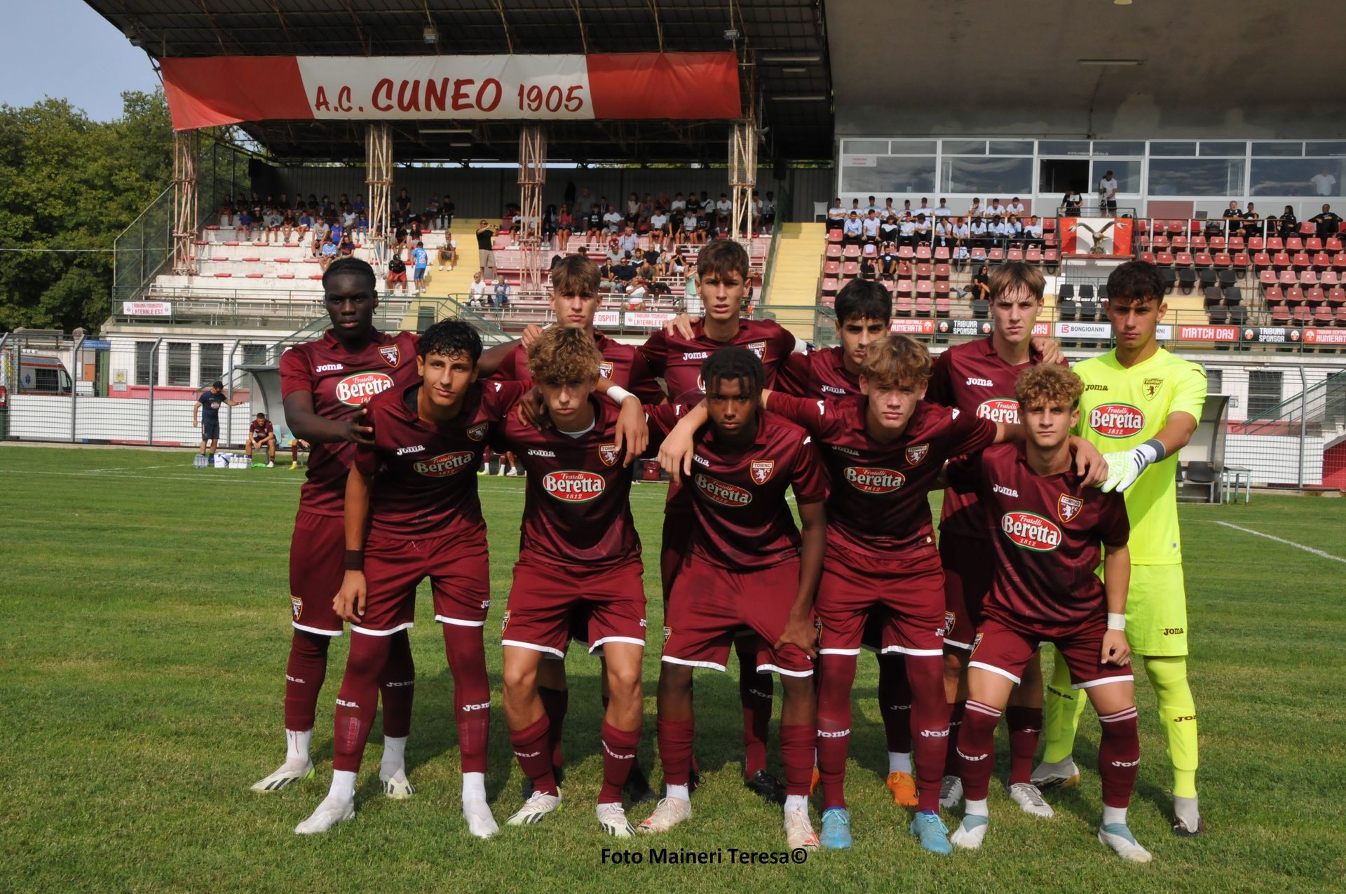 Squadra di calcio in uniforme marrone in posa su un campo verde di fronte a uno stadio.
