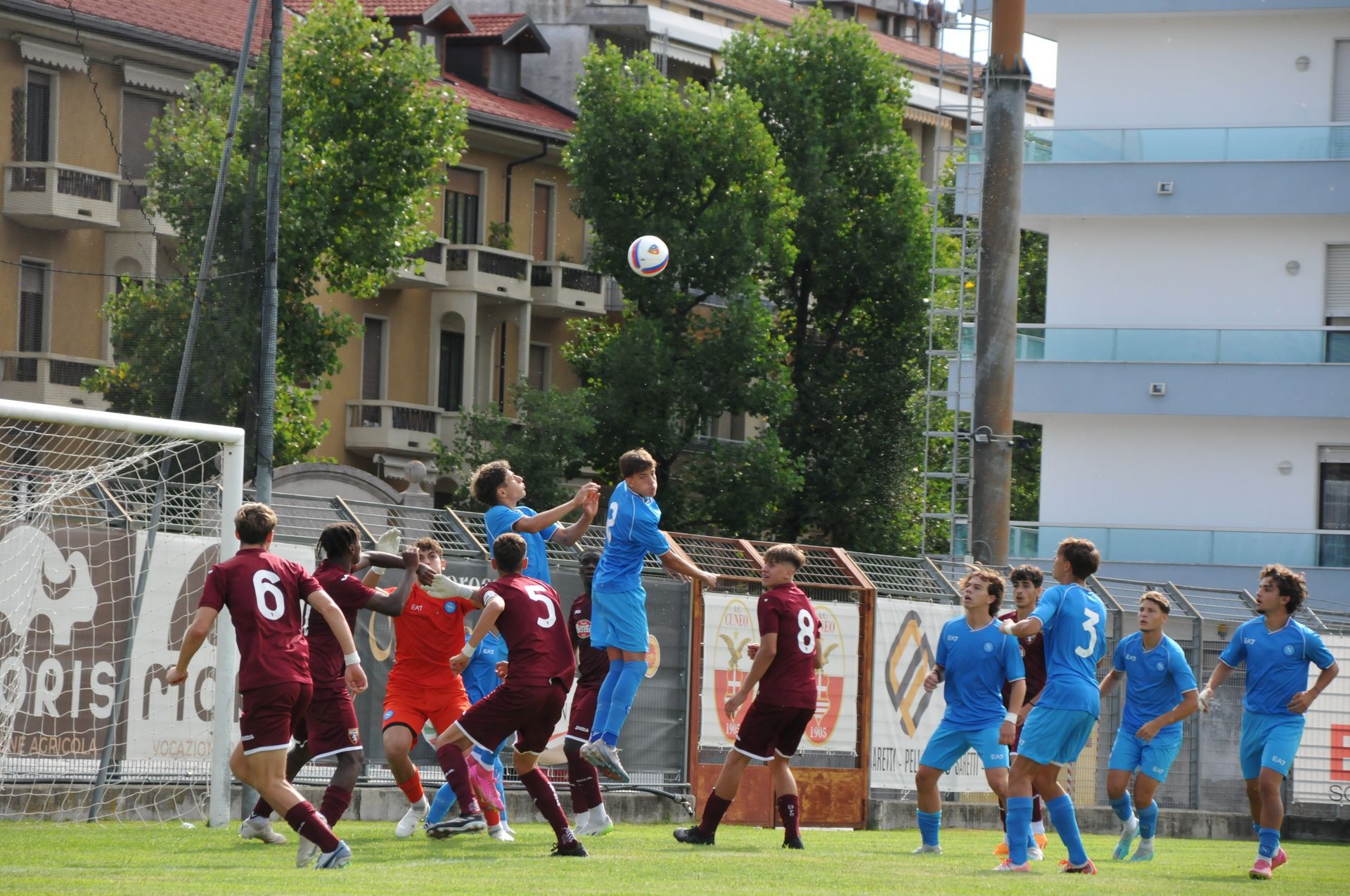 Calciatori in azione, che saltano per prendere la palla durante una partita. Maglie rosse e blu su un campo verde.