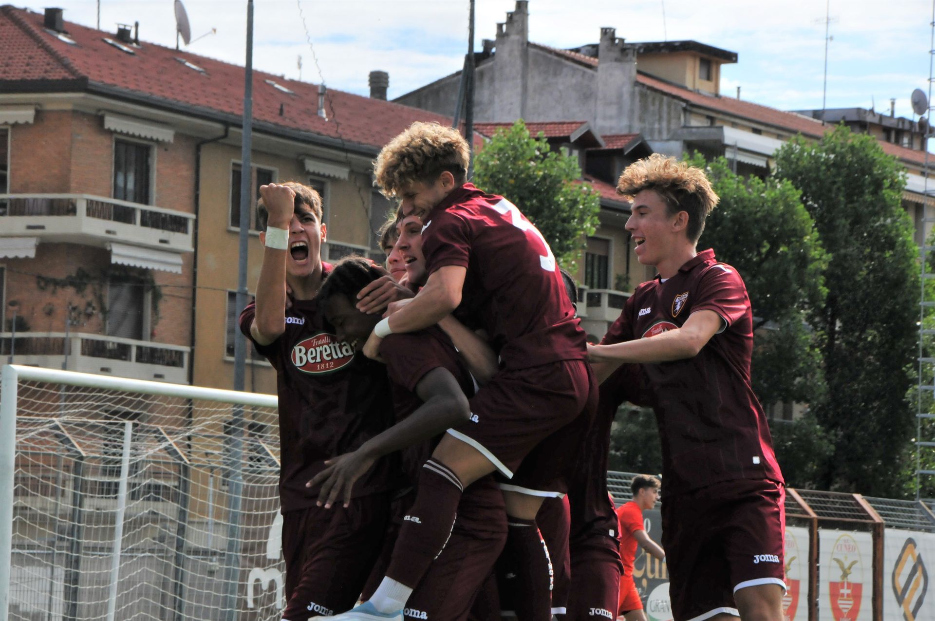 I calciatori in uniforme marrone festeggiano un gol, saltando e abbracciandosi sul campo.