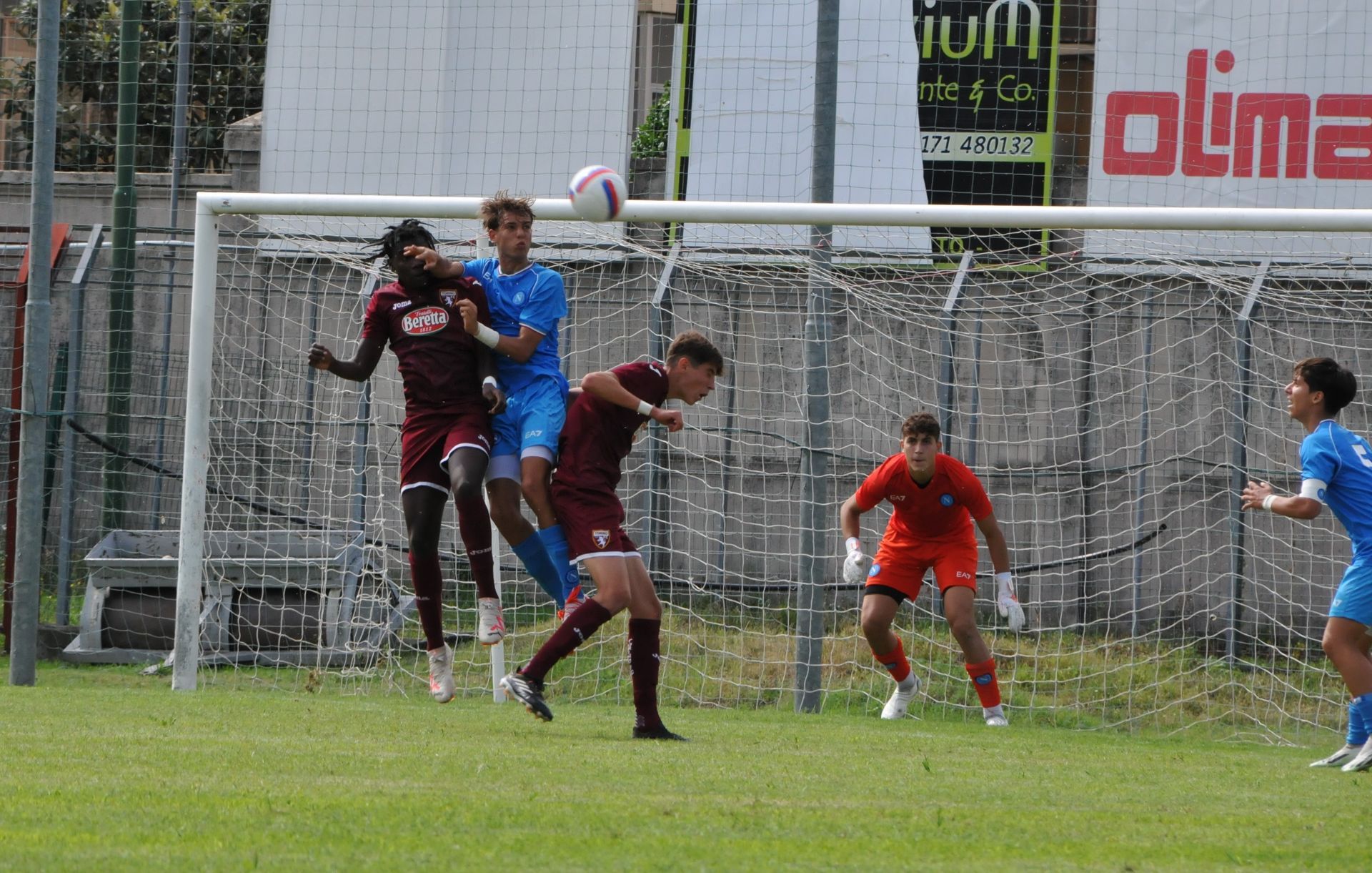 Giocatori di calcio in divisa bordeaux e blu, che colpiscono la palla di testa vicino alla porta.