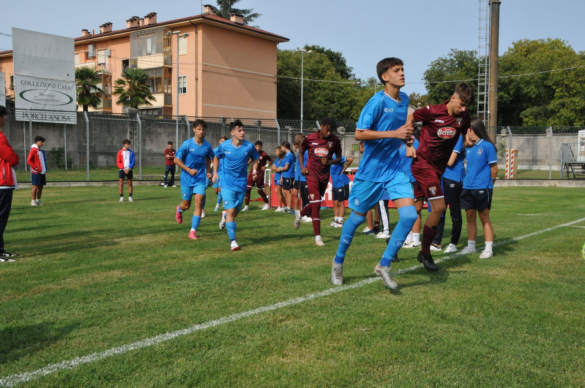 Giocatori di calcio con maglie blu e bordeaux che corrono su un campo verde.