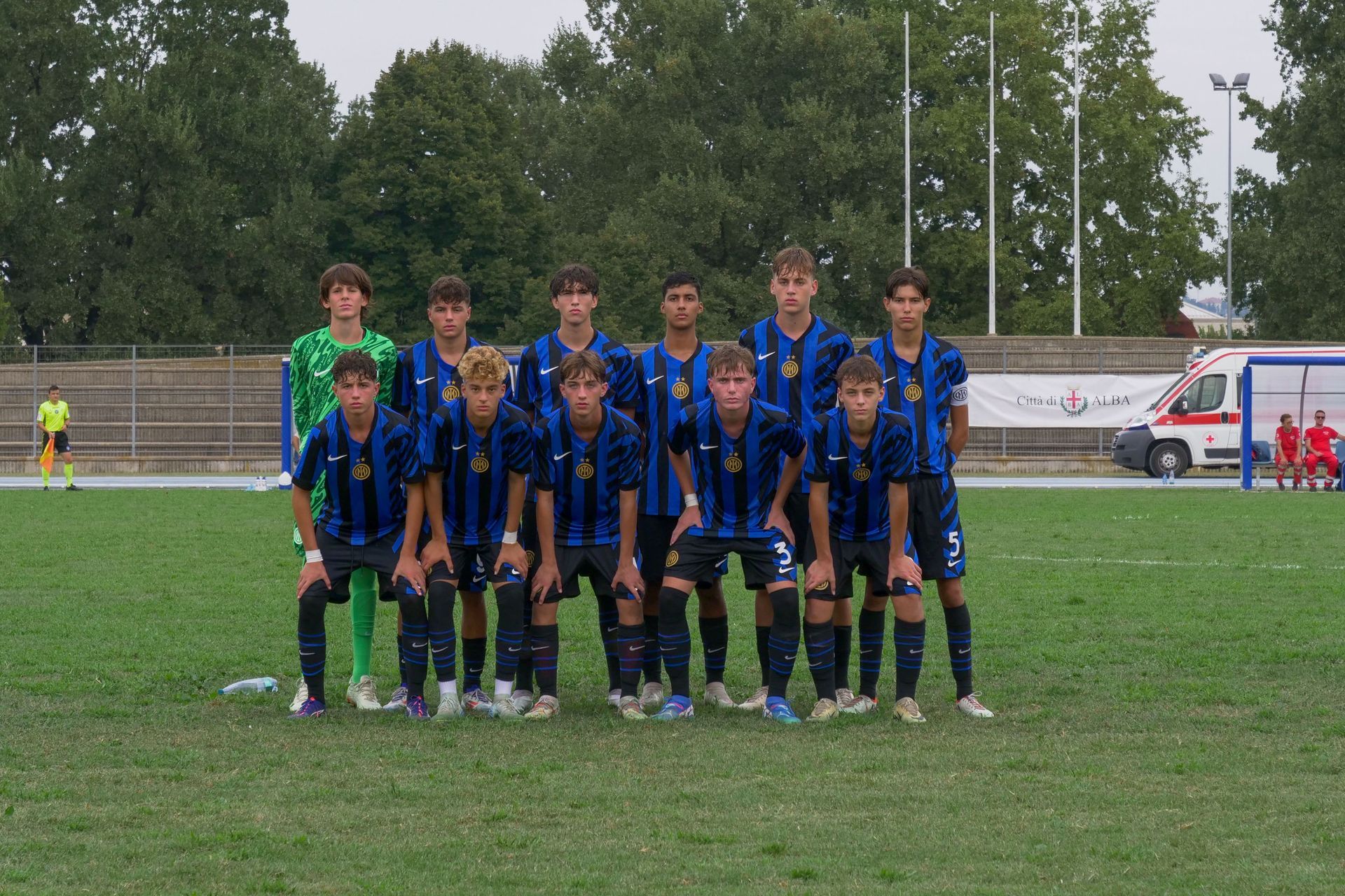 Squadra di calcio in maglia blu e nera inginocchiata su un campo verde. I giocatori posano per una foto.
