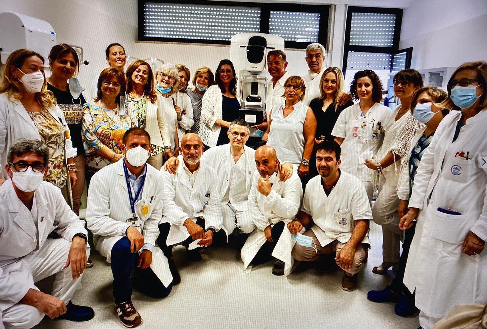 Gruppo di persone in camice da laboratorio in posa vicino ad apparecchiature mediche in una stanza ben illuminata.