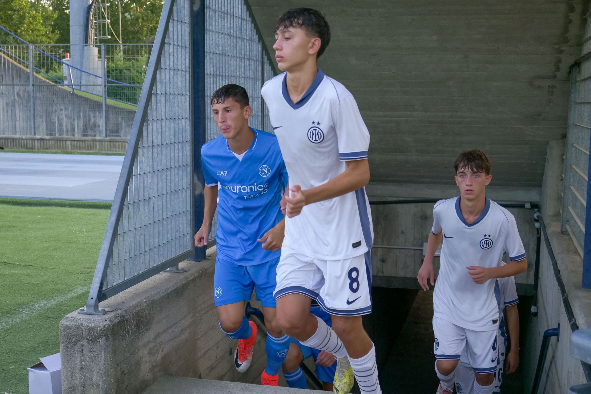 I giocatori di calcio in divisa bianca e blu salgono di corsa i gradini che conducono al tunnel dello stadio.