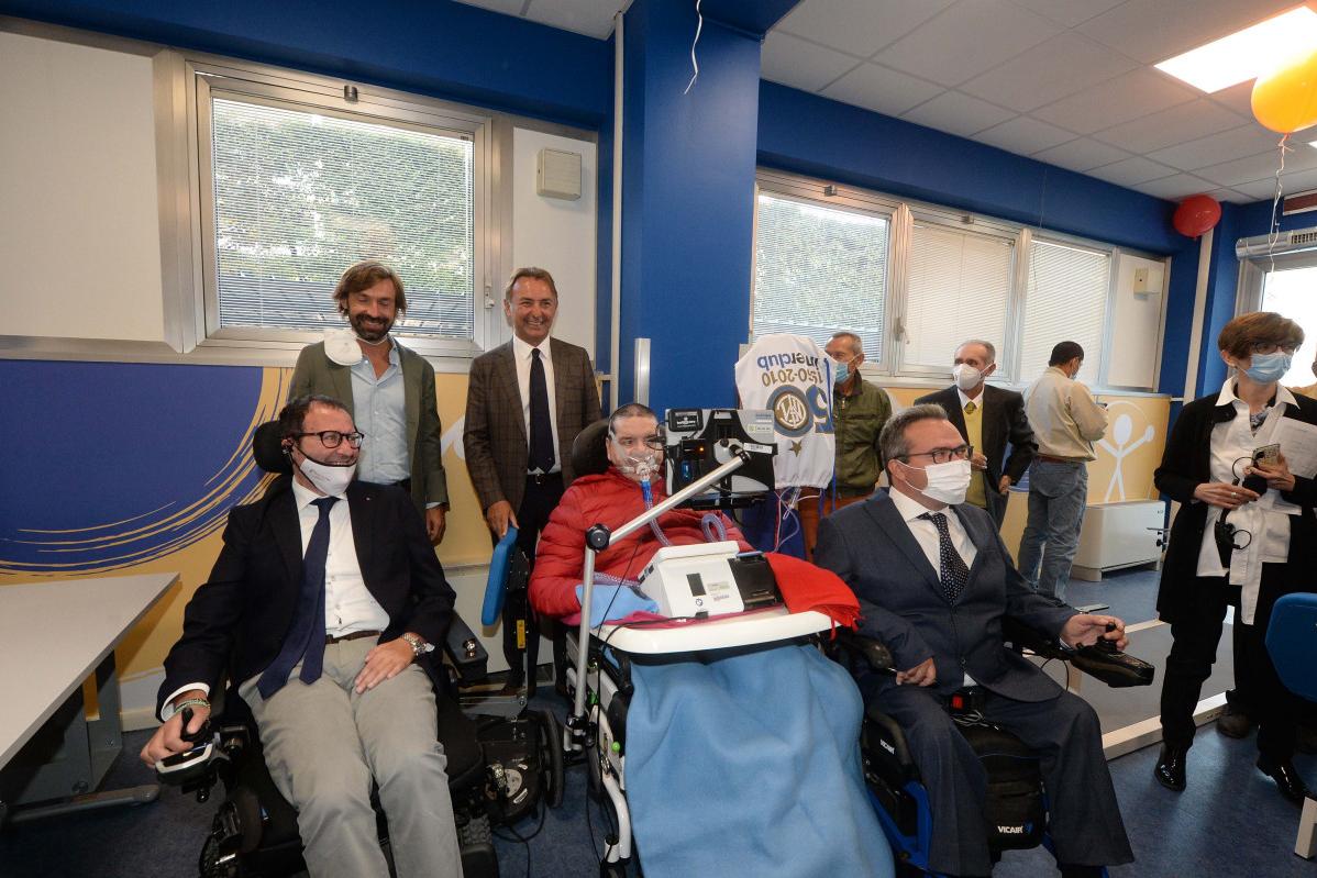 Foto di gruppo a un evento: persone in giacca e cravatta con persone in sedia a rotelle; sala blu e gialla.