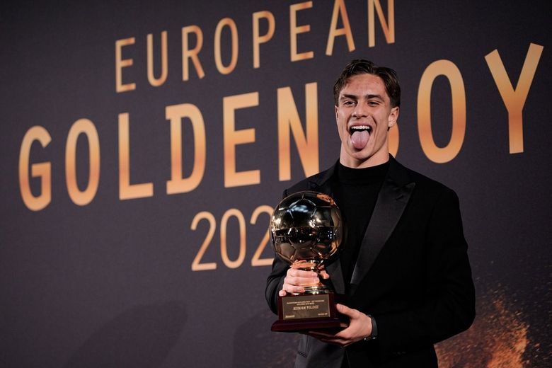 Uomo che tiene in mano il trofeo Golden Boy, tirando fuori la lingua, davanti al cartello 