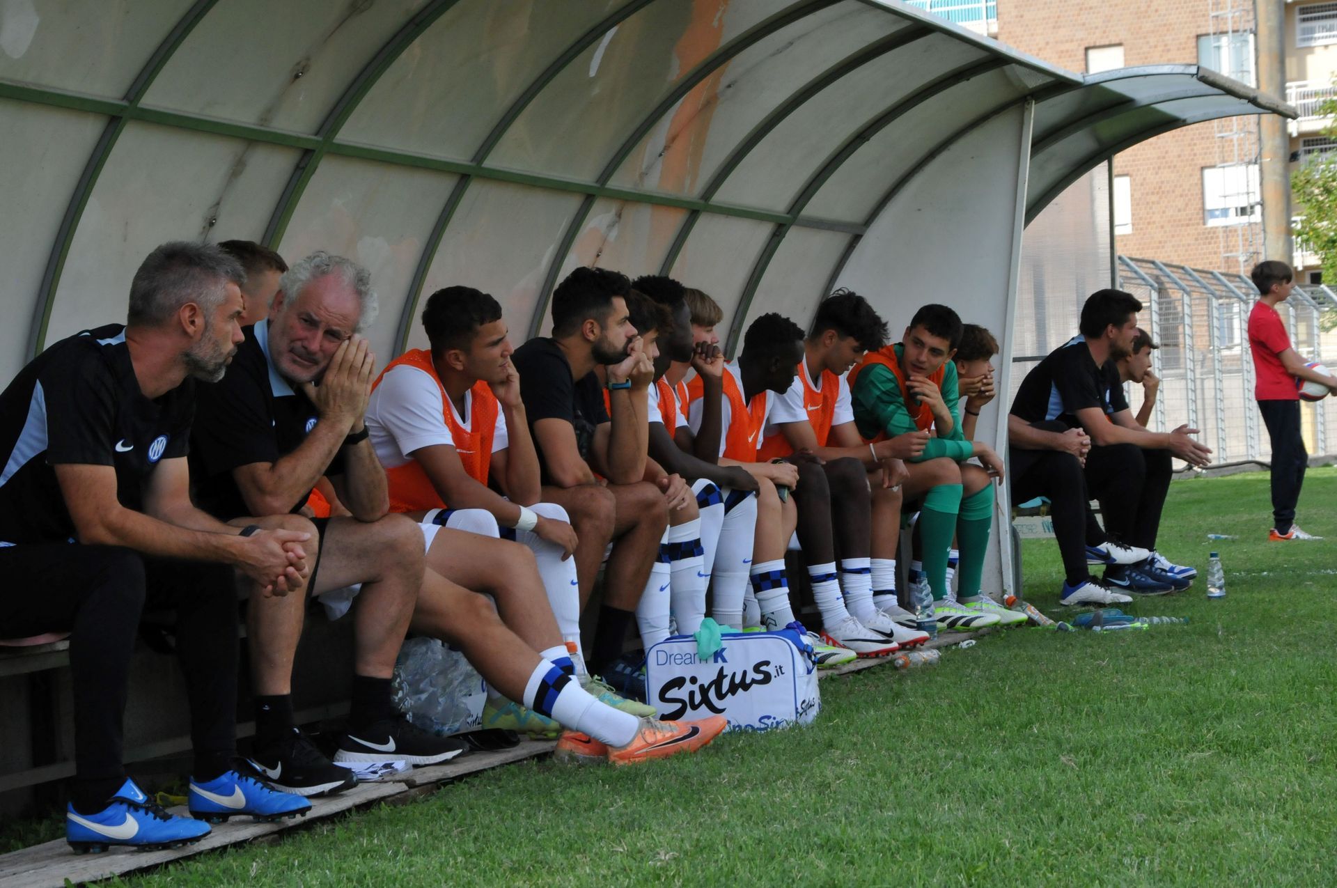 I sostituti della squadra di calcio sono seduti su una panchina e guardano la partita. Campo verde, giornata di sole.