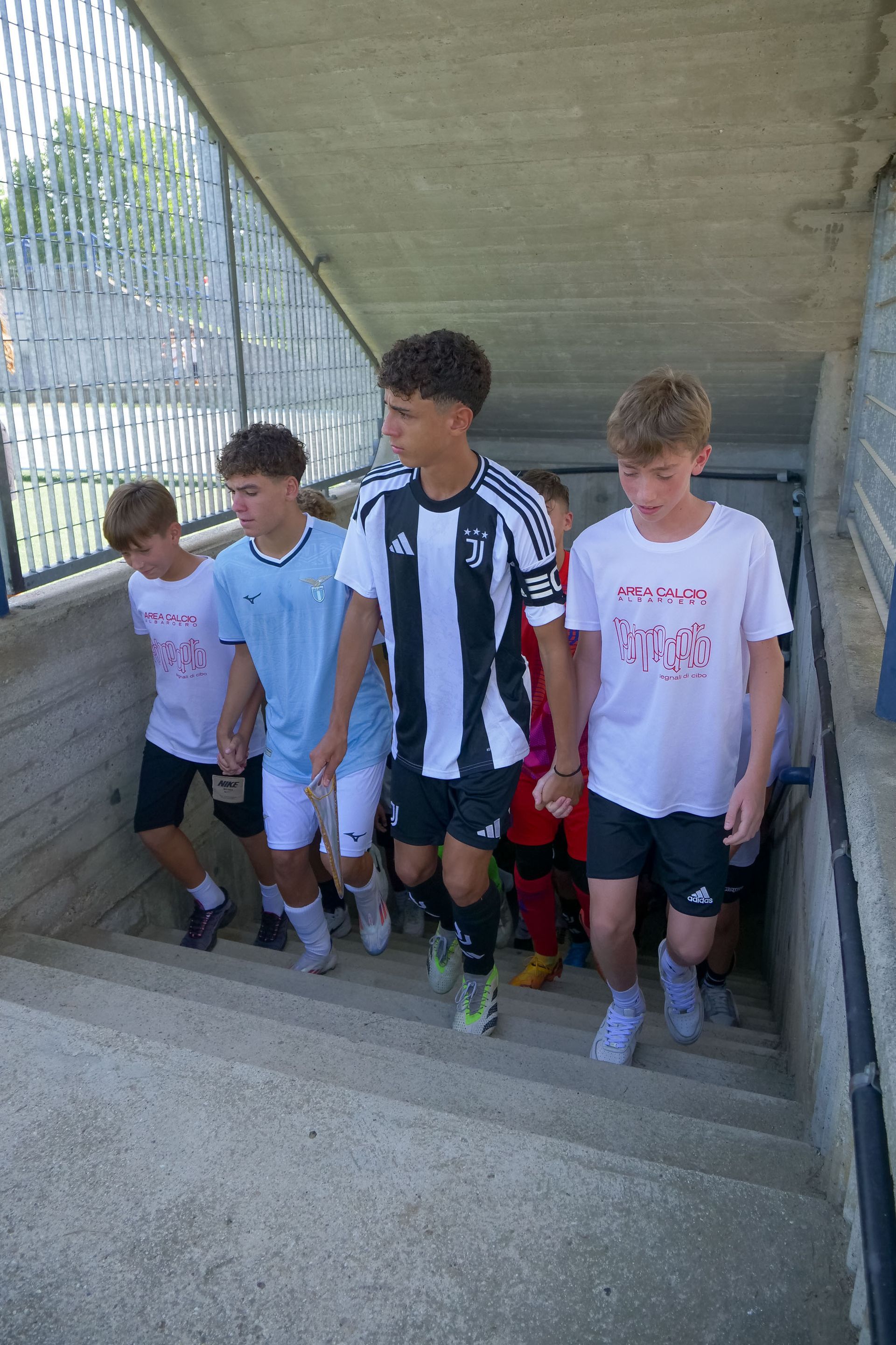Gruppo di giovani che salgono le scale di pietra; uno di loro indossa una divisa da calcio.