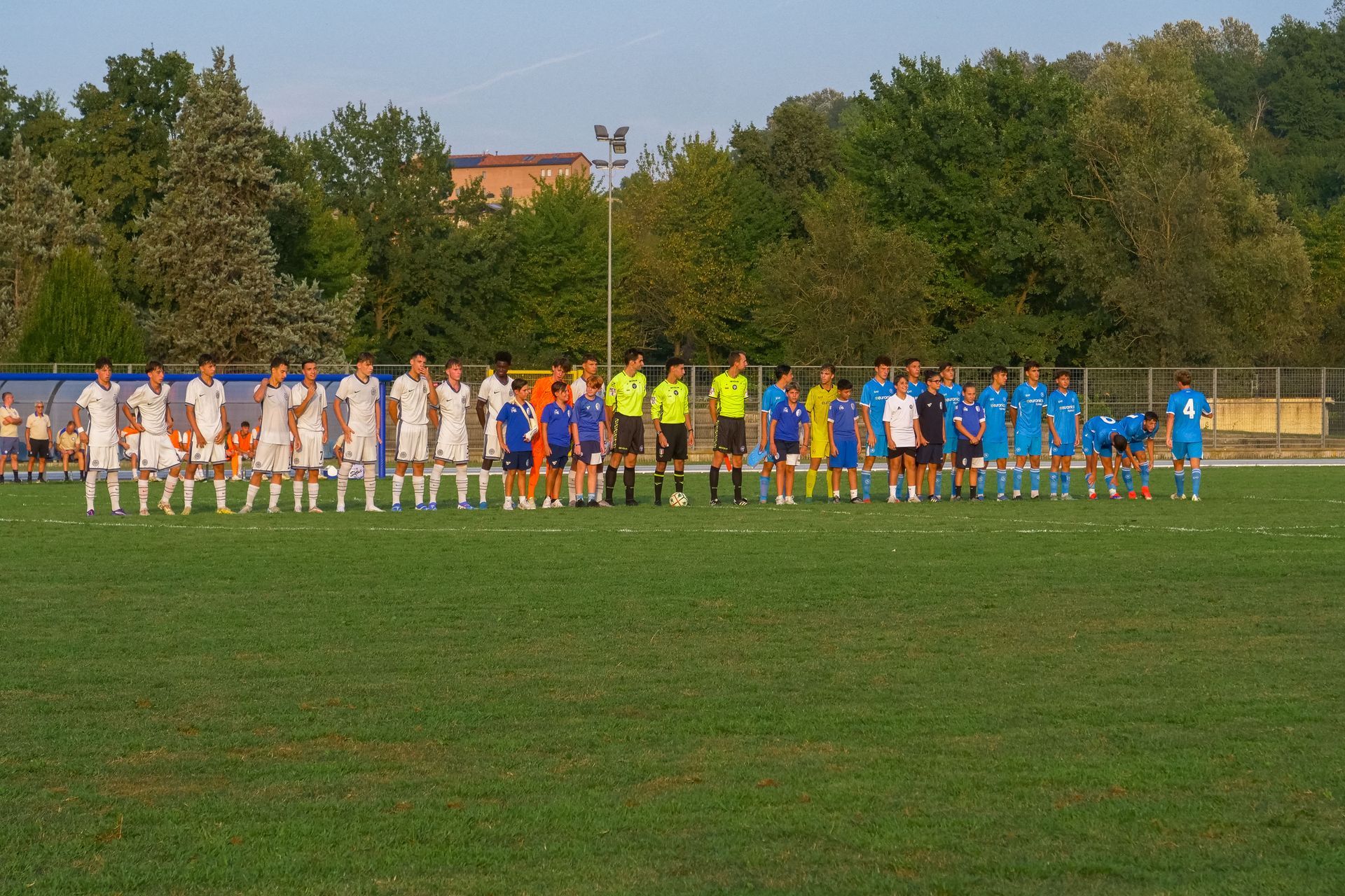 Le squadre di calcio, in divisa bianca e blu, si affrontano su un campo verde prima di una partita.