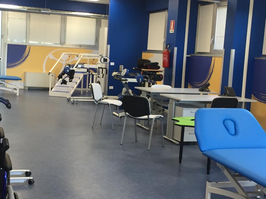 Sala per la terapia con pavimento e pareti blu, attrezzi ginnici, tavoli e sedie.