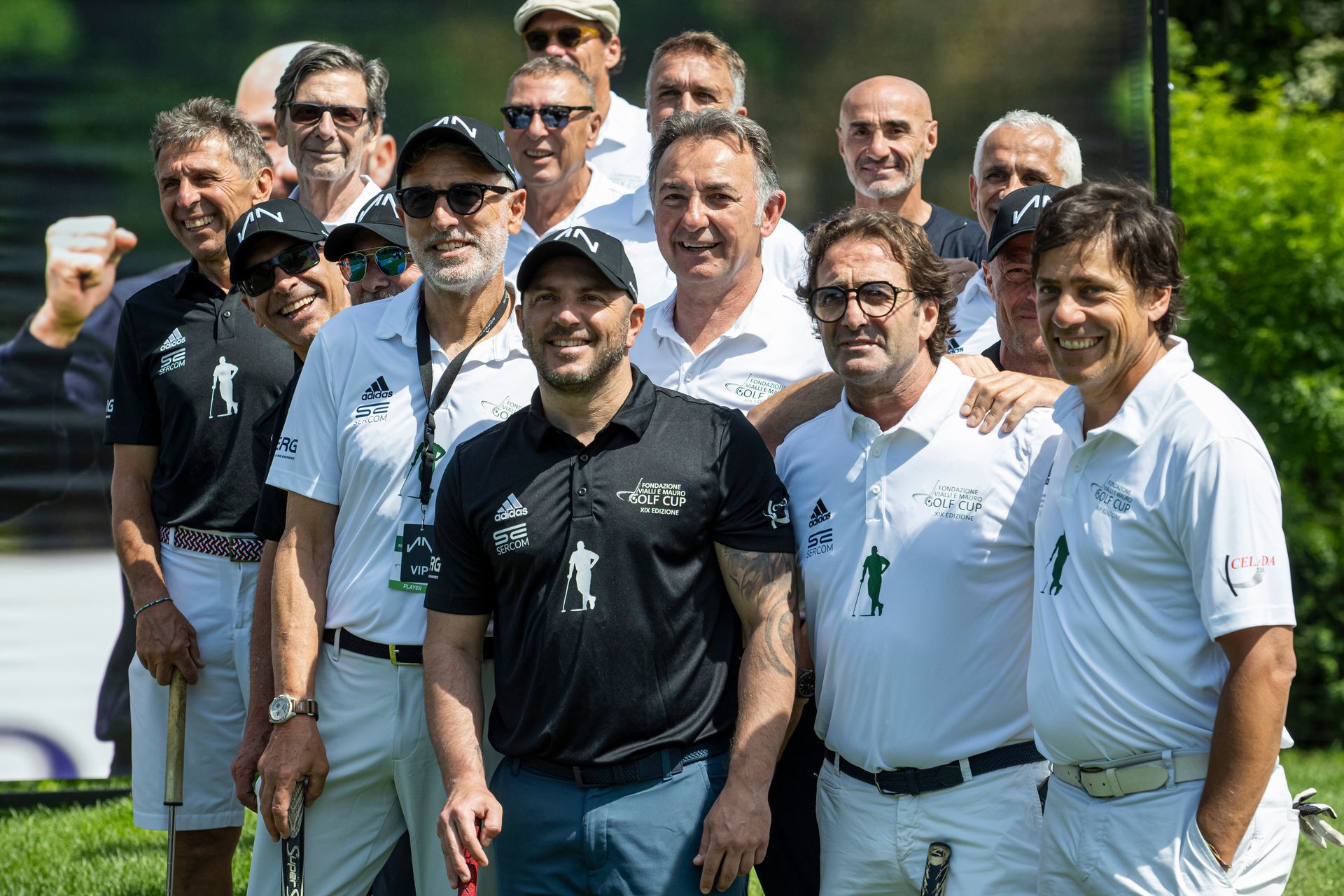 Un gruppo di uomini, per lo più in polo bianca, posa all'aperto. Alcuni tengono in mano delle mazze da golf, sorridenti.