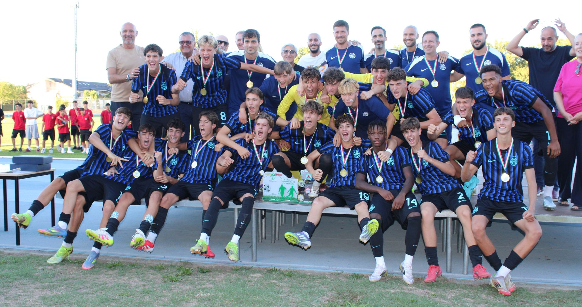 La squadra di calcio con le maglie blu festeggia con le medaglie su un podio all'aperto.