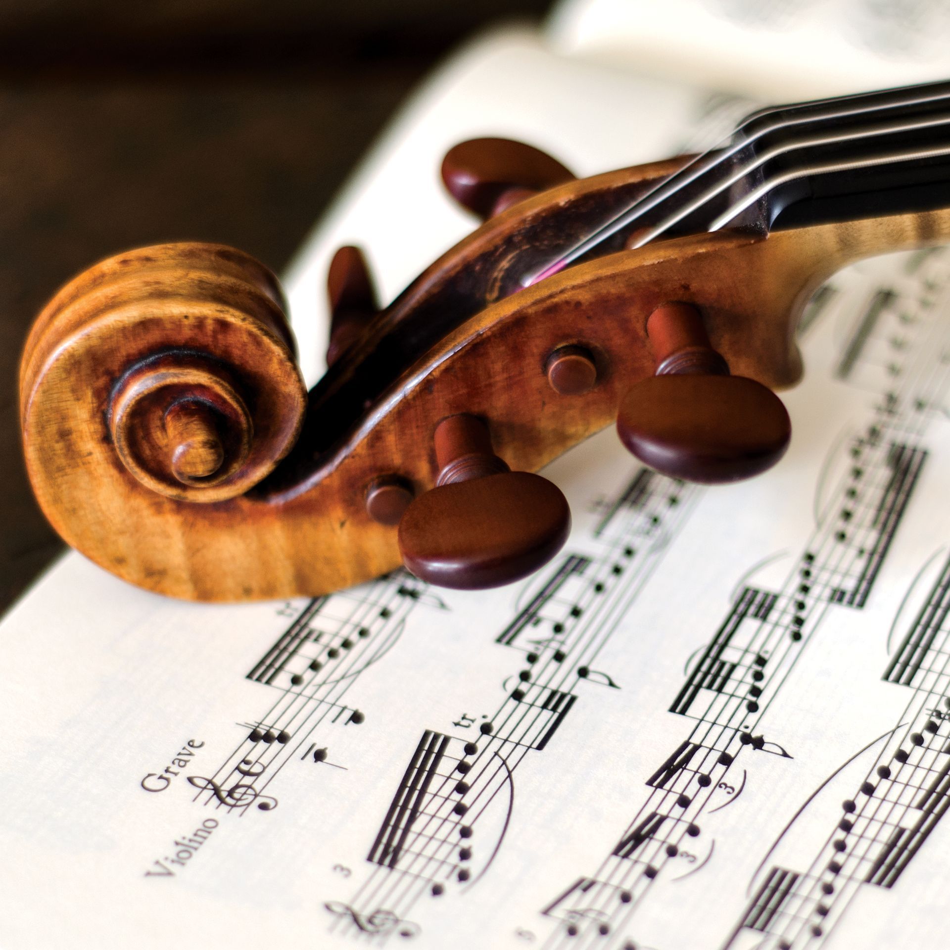 Primo piano della paletta di un violino sopra uno spartito con note musicali.