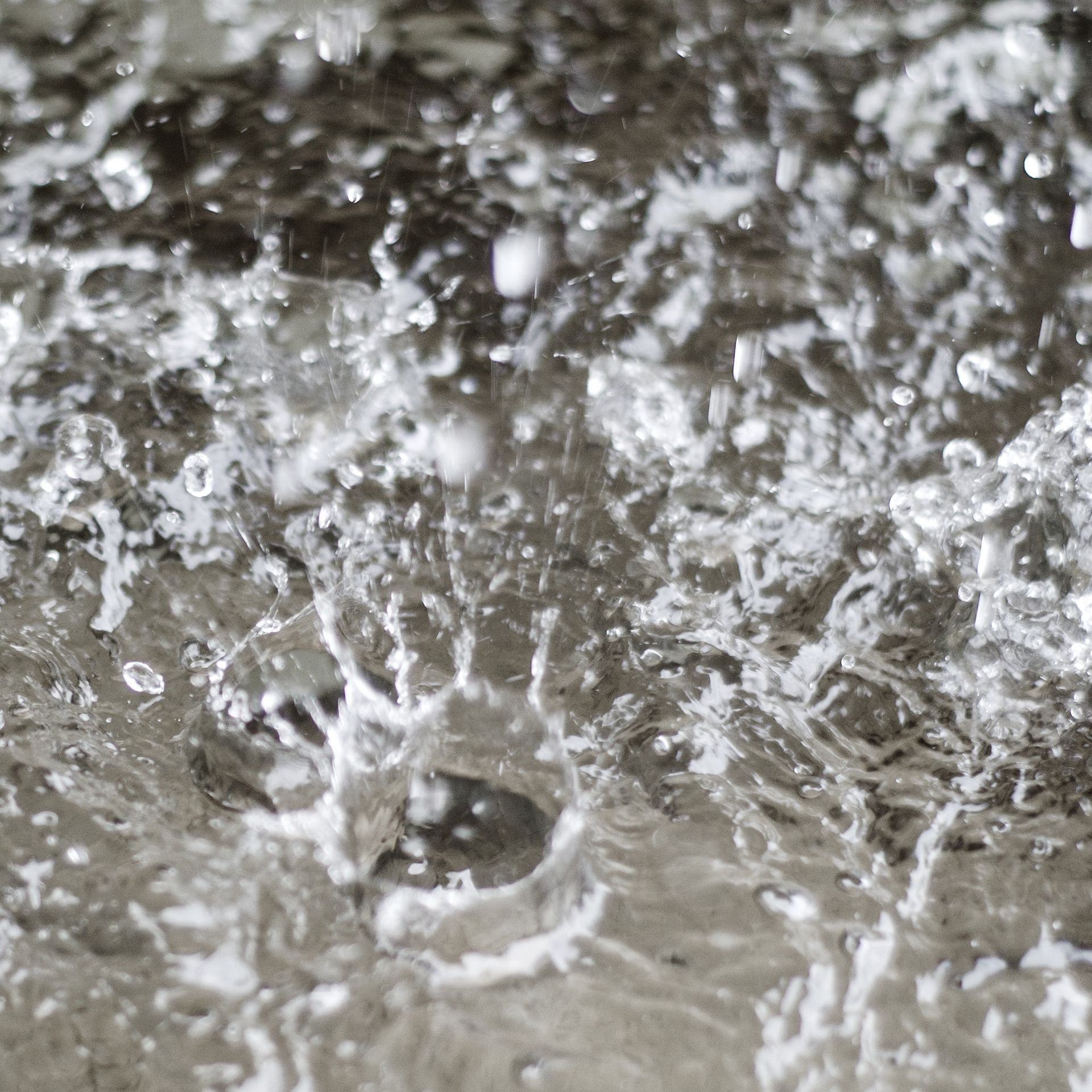 Acqua che schizza, creando goccioline e increspature su una superficie grigia.