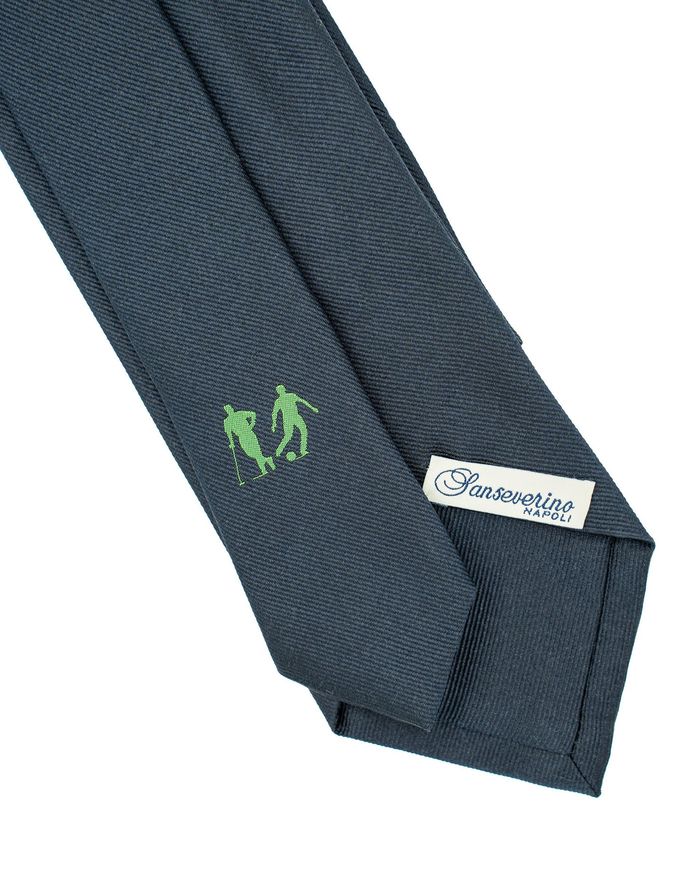 Cravatta blu con figure ricamate in verde ed etichetta bianca.