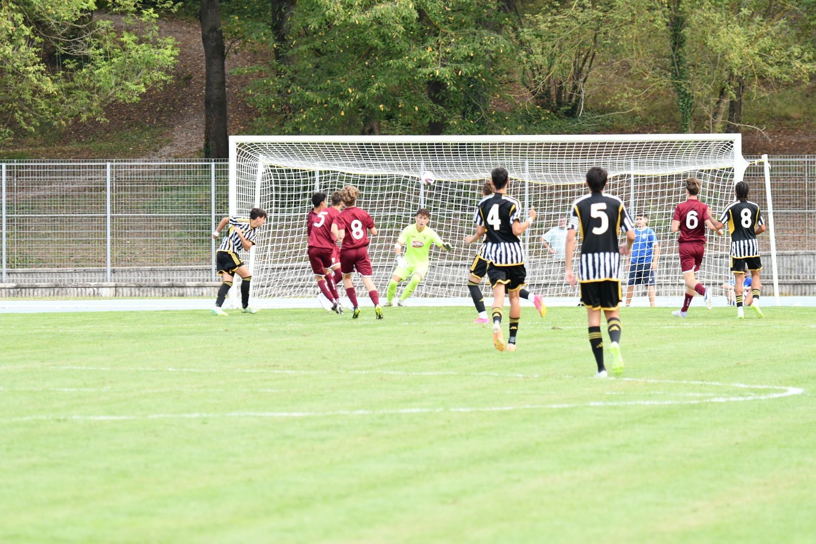 Azione di una partita di calcio: giocatori con strisce bianche e nere e maglie color marrone vicino alla porta su un campo verde.