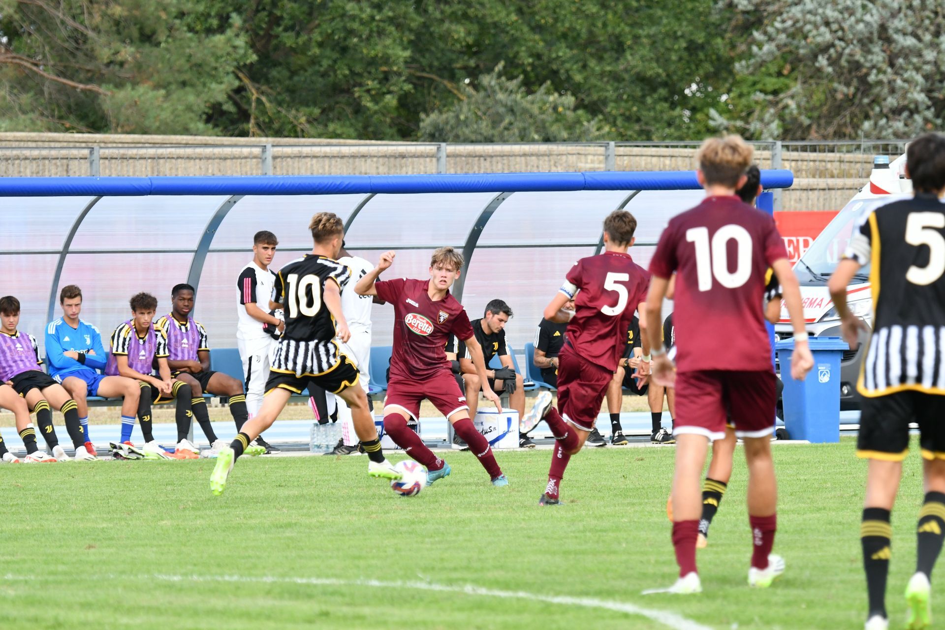 Giocatori di calcio in divise bordeaux e nere su un campo verde. I giocatori corrono e calciano la palla.