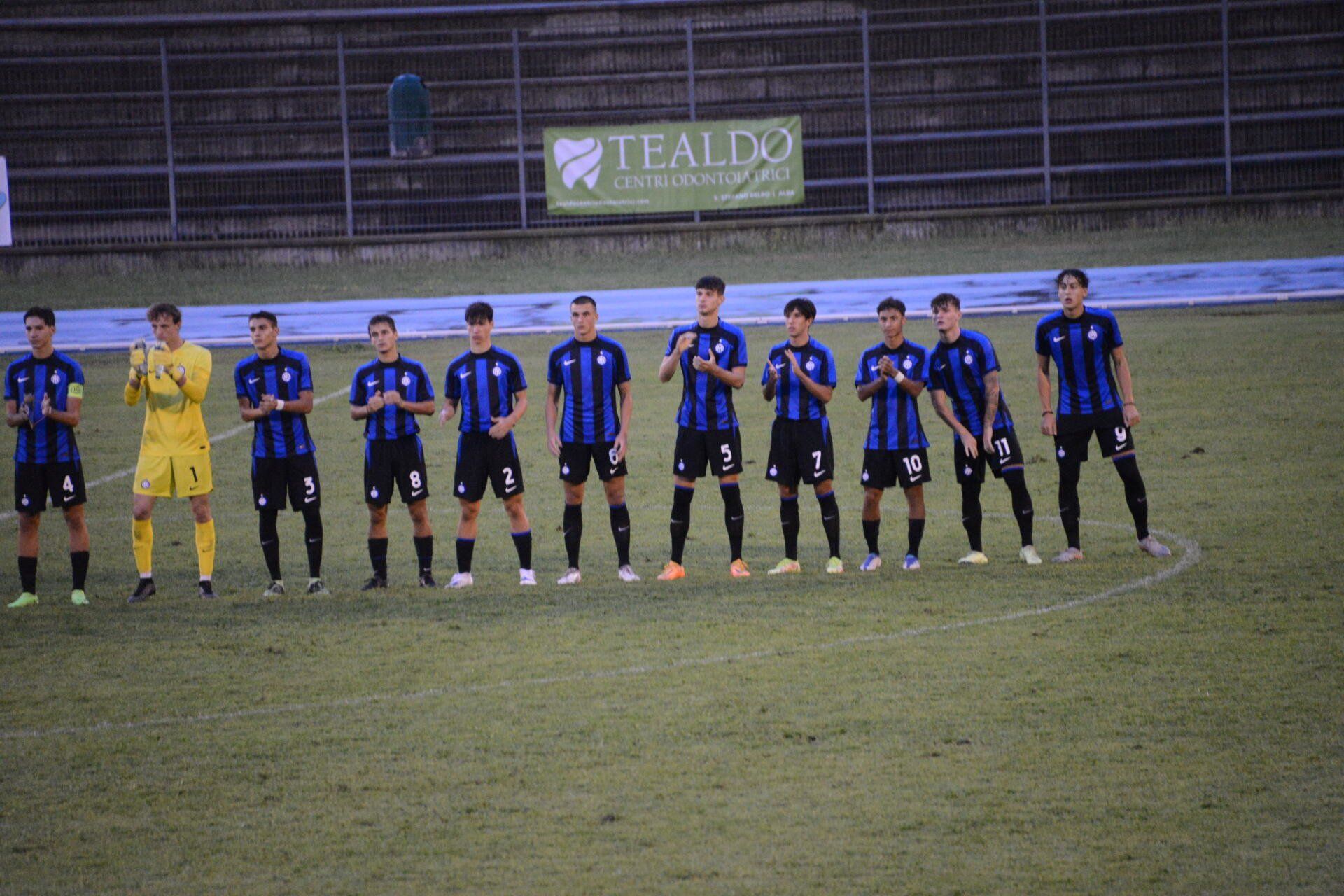 Squadra di calcio in divisa blu e nera su un campo verde. Giocatori in piedi, alcuni applaudono.